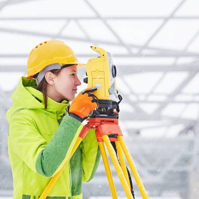 female surveyor worker working with theodolite transit equipment at road construction site outdoors